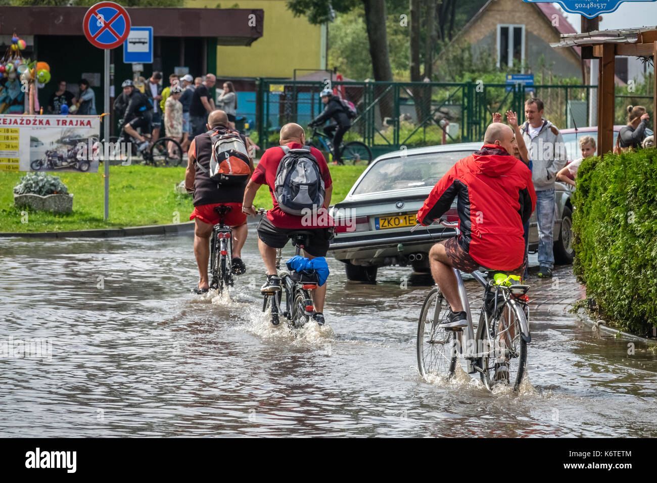 Sarbinowo, Pologne - août 2017 : trois hommes à vélo dans une eau profonde sur une route inondée après une pluie torrentielle Banque D'Images
