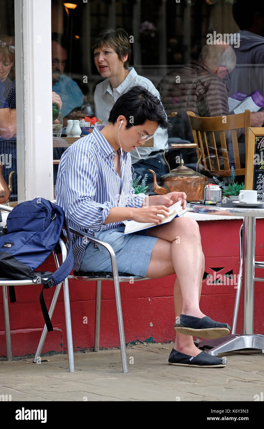 Jeune homme assis à l'extérieur cafe reading book, Cambridge, Angleterre Banque D'Images