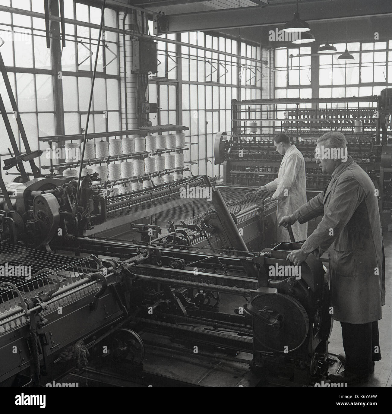 Années 1950, historique, photo, représentant des hommes dans des combinaisons complexes de grande envergure de travail machines mécaniques, un spinner et spinning mule dans une filature de laine peignée prix, Leeds, Angleterre, Royaume-Uni. La laine peignée fine est un bon tissu fait de longs fils de fil de laine et le processus spining est plus lente. Banque D'Images