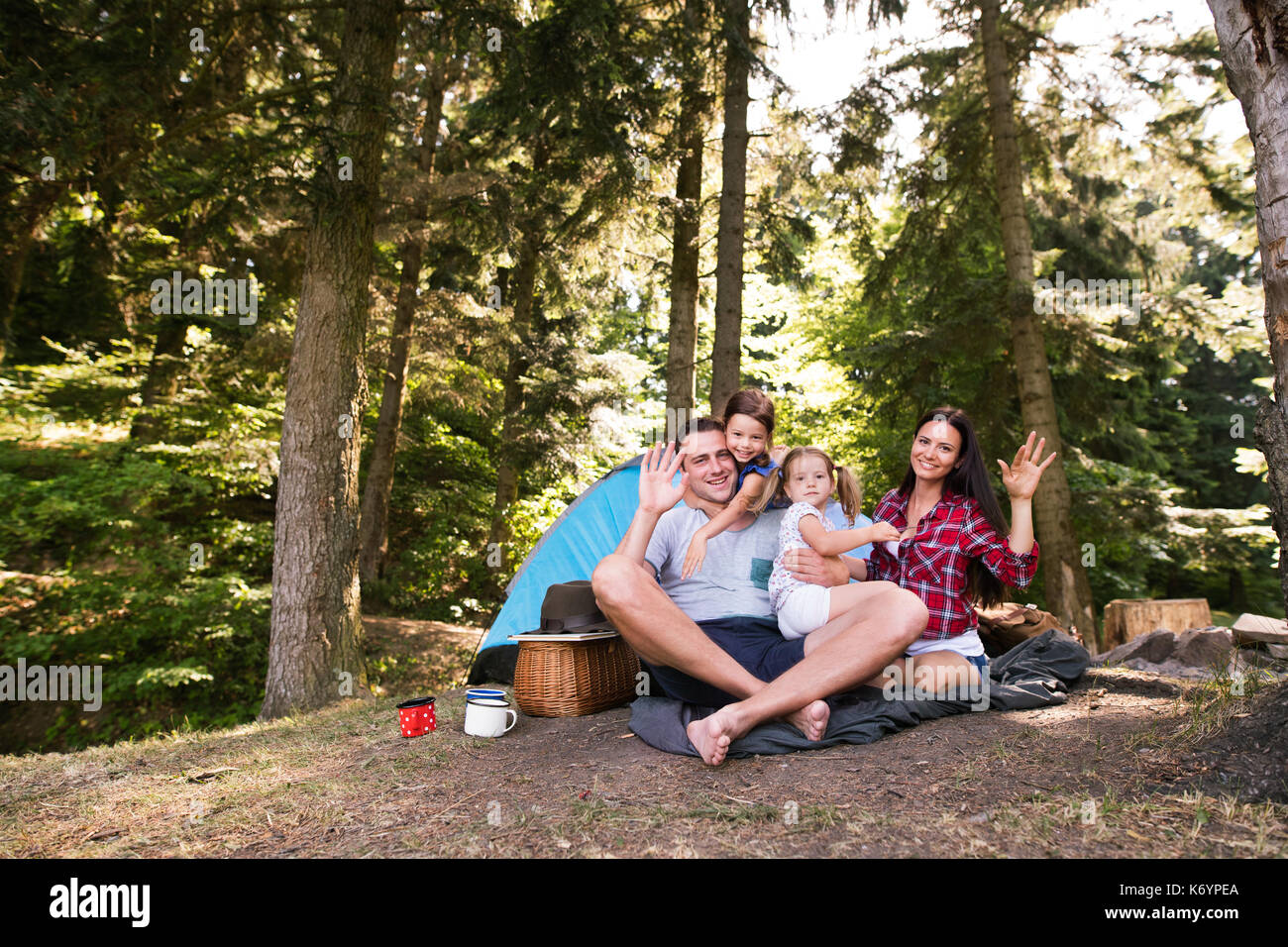 Beau jeune famille avec mignon filles du camping en forêt, assis en face de la tente. Banque D'Images