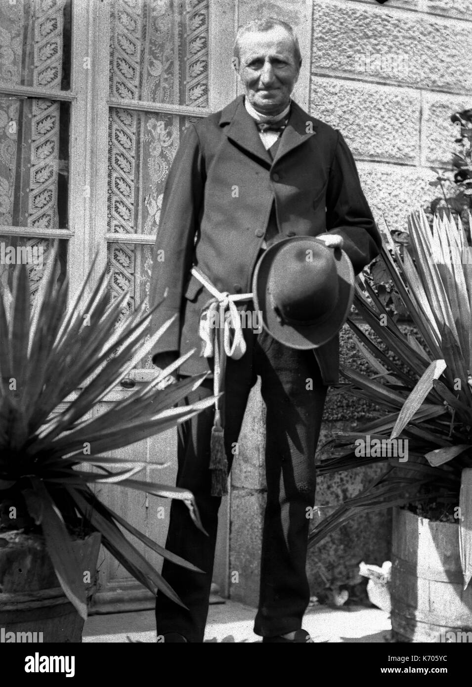 AJAXNETPHOTO. 1891-1910 (environ). La France. - PORTRAIT D'un vieux monsieur tenant un chapeau portant une ceinture à l'extérieur DEBOUT EN FACE D'UNE FENÊTRE DE LA CHAMBRE ENTRE LES PLANTES EN POTS. Photographe:Inconnu © COPYRIGHT DE L'IMAGE NUMÉRIQUE PHOTO VINTAGE AJAX AJAX BIBLIOTHÈQUE SOURCE : VINTAGE PHOTO LIBRARY COLLECTION REF:AVL  FRA 1890 B29X1227 Banque D'Images