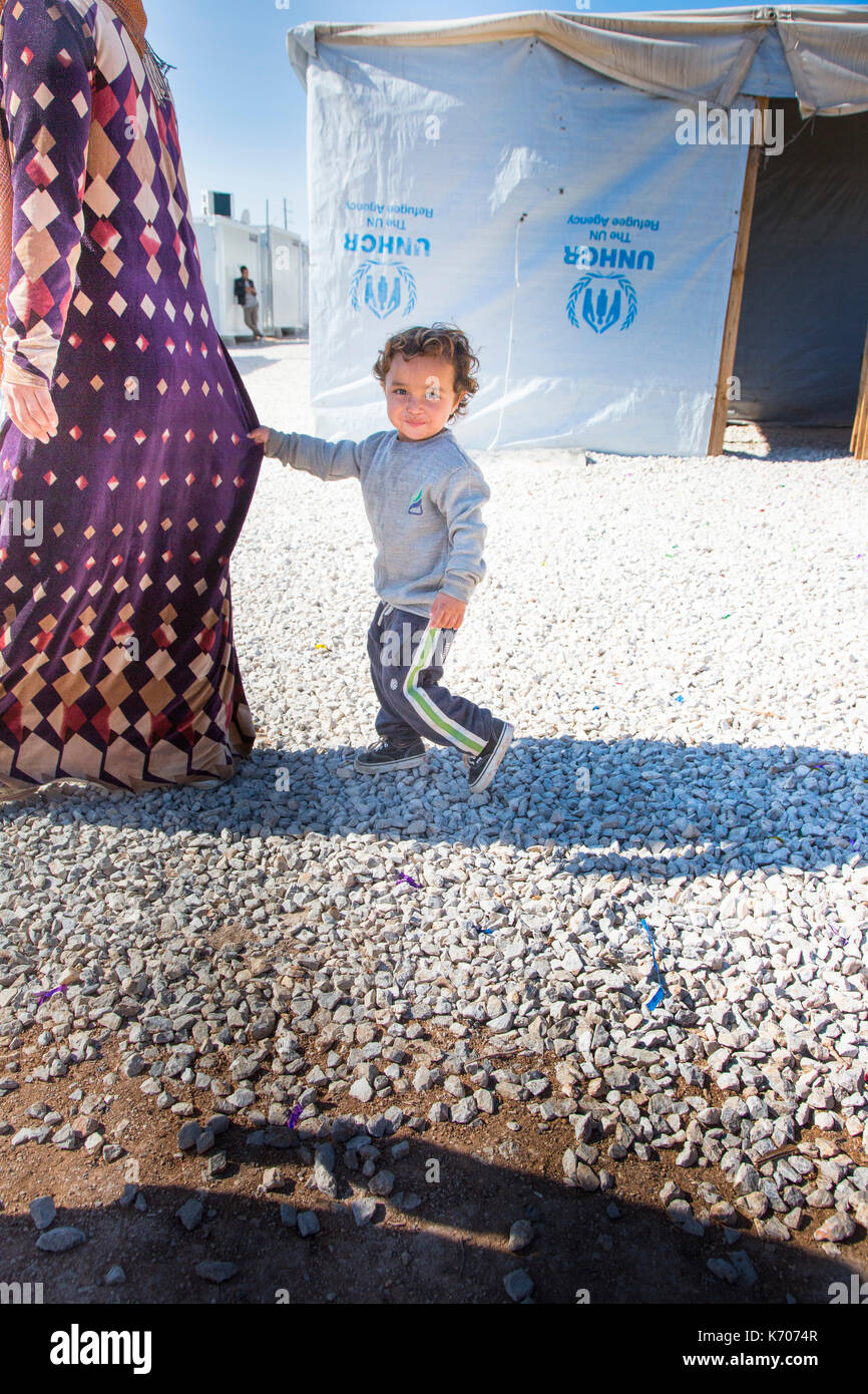 Comme ils passent devant des rangées de maisons d'urgence, un garçon est titulaire sur la robe de sa mère. Elle marche en tant qu'il est distrait et regarde dans d'autres directions. Banque D'Images