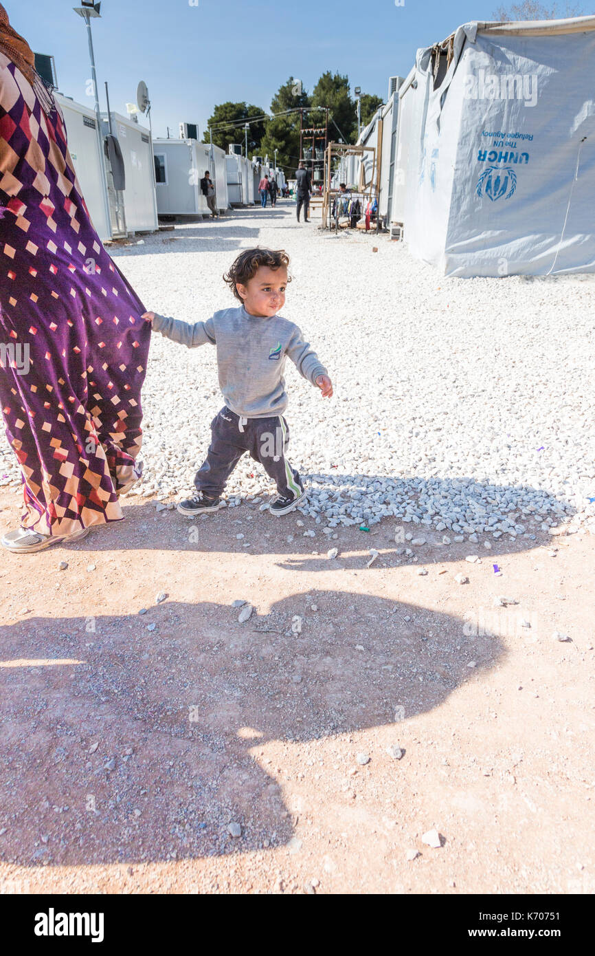 Comme ils passent devant des rangées de maisons d'urgence, un garçon est titulaire sur la robe de sa mère. Elle marche en tant qu'il est distrait et regarde dans d'autres directions. Banque D'Images