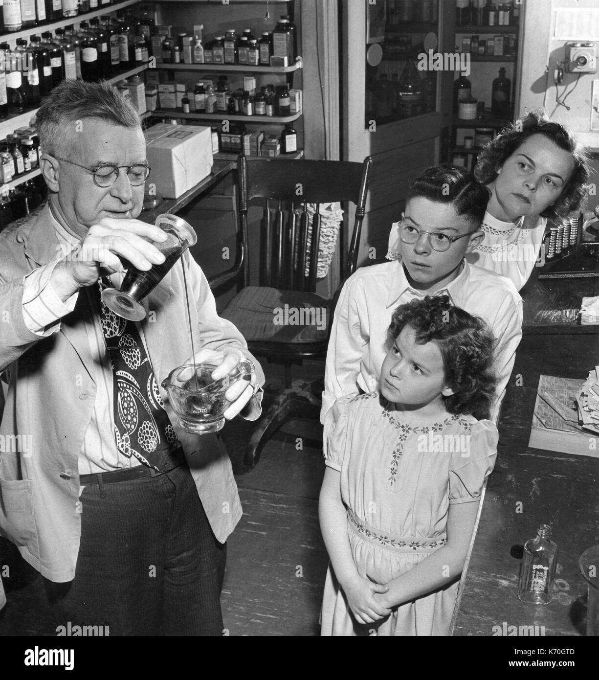 Les enfants anxieux regarder un pharmacien mix médecine. 1949, New York. Banque D'Images