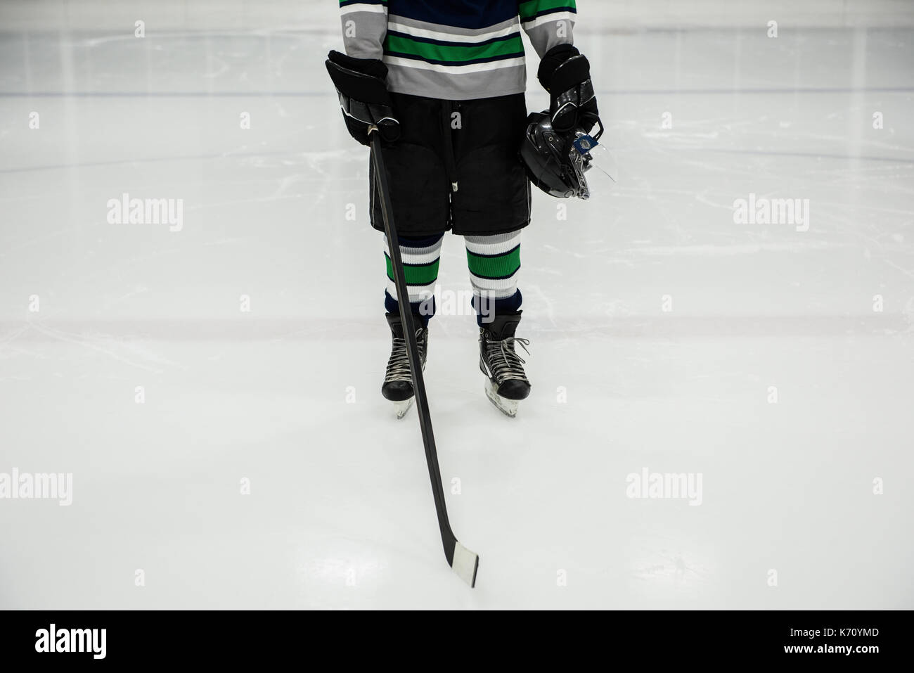 La section basse de l'homme joueur tenant le bâton de hockey sur glace et casque en rink Banque D'Images