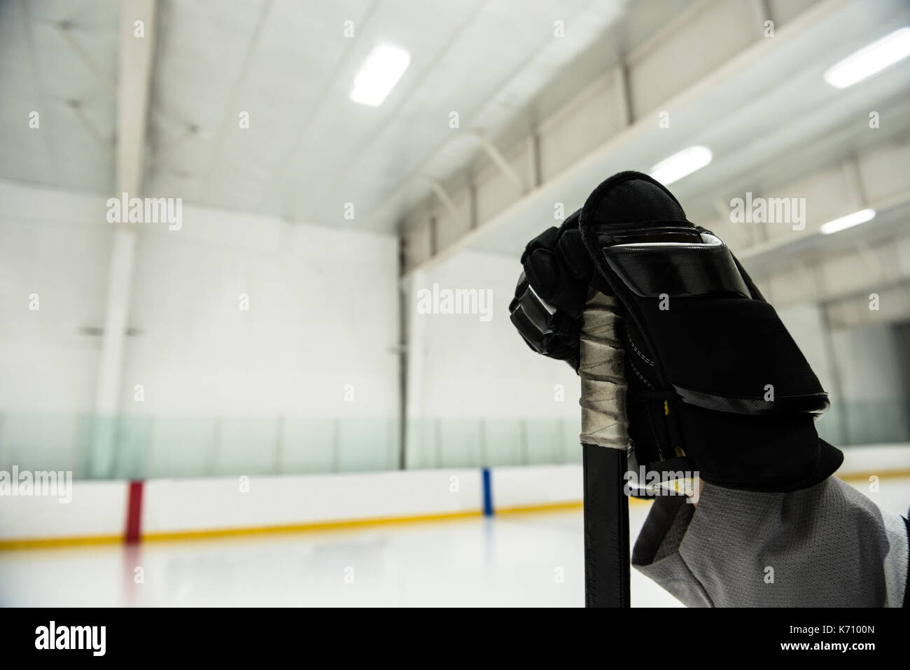 Cropped hand of male joueur tenant le bâton de hockey sur glace à la patinoire éclairée Banque D'Images