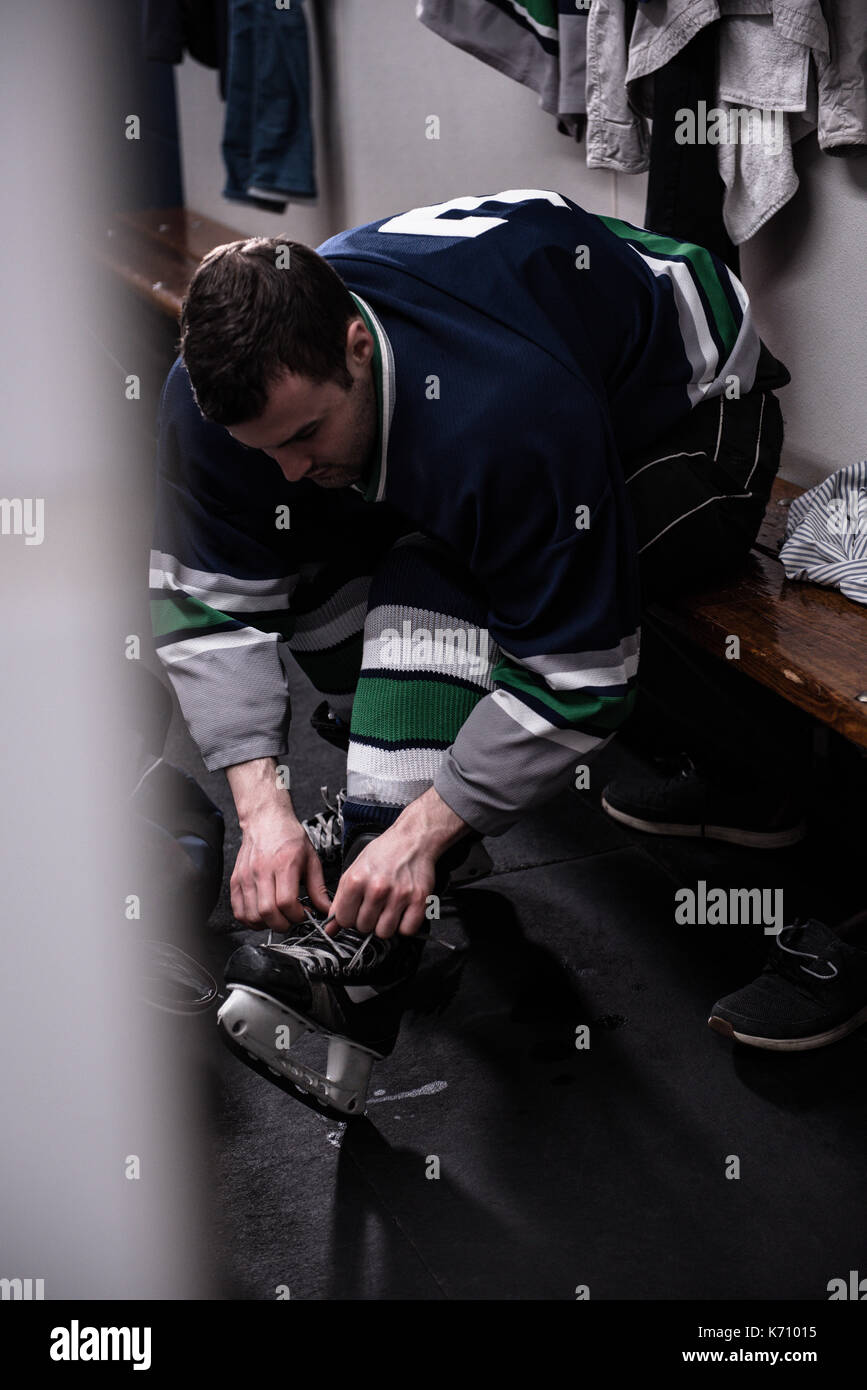 Joueur de hockey sur glace masculin de patinage de liage en position assise en dressing Banque D'Images