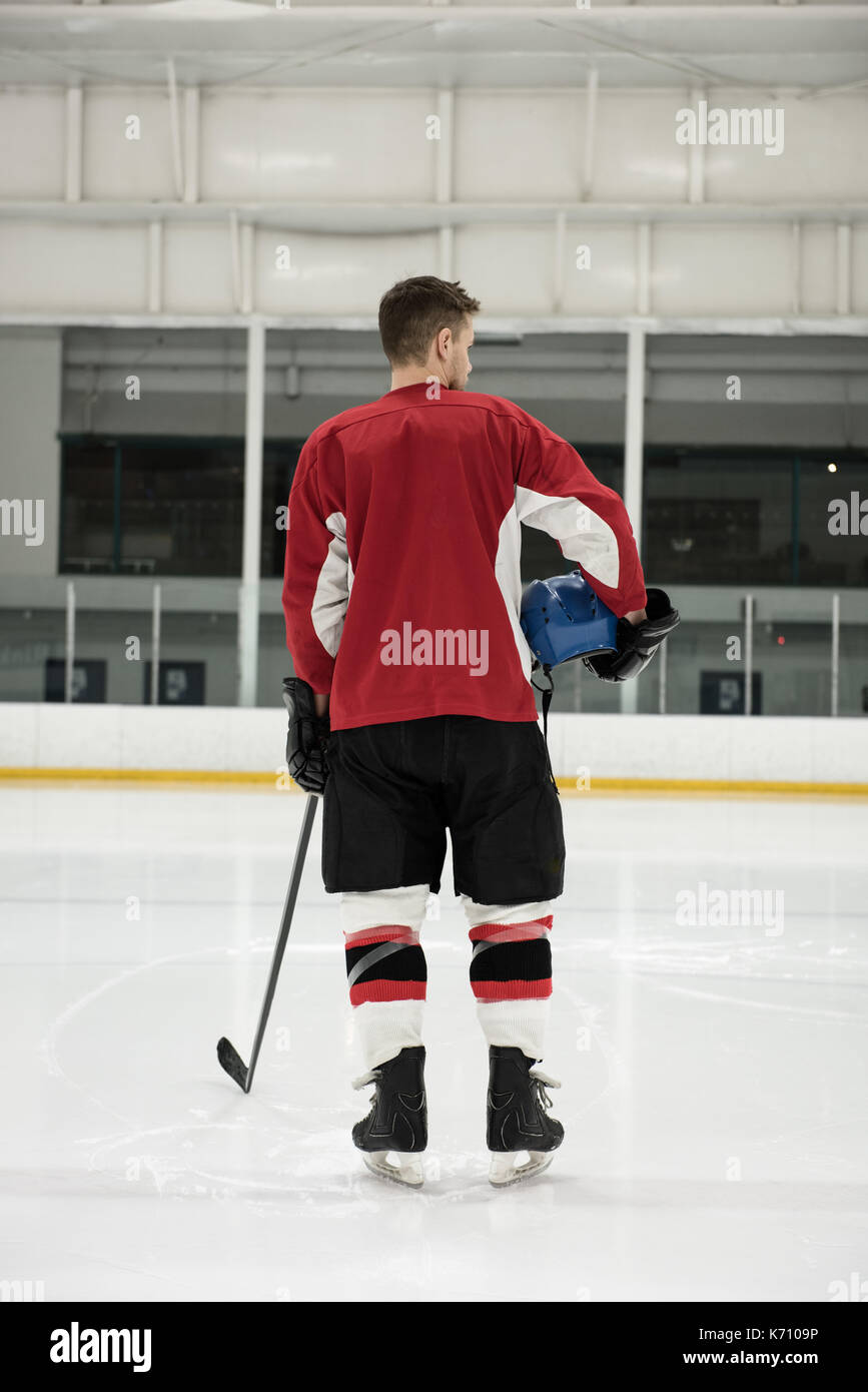 Vue arrière du joueur de hockey sur glace masculin holding helmet et bâton à rink Banque D'Images