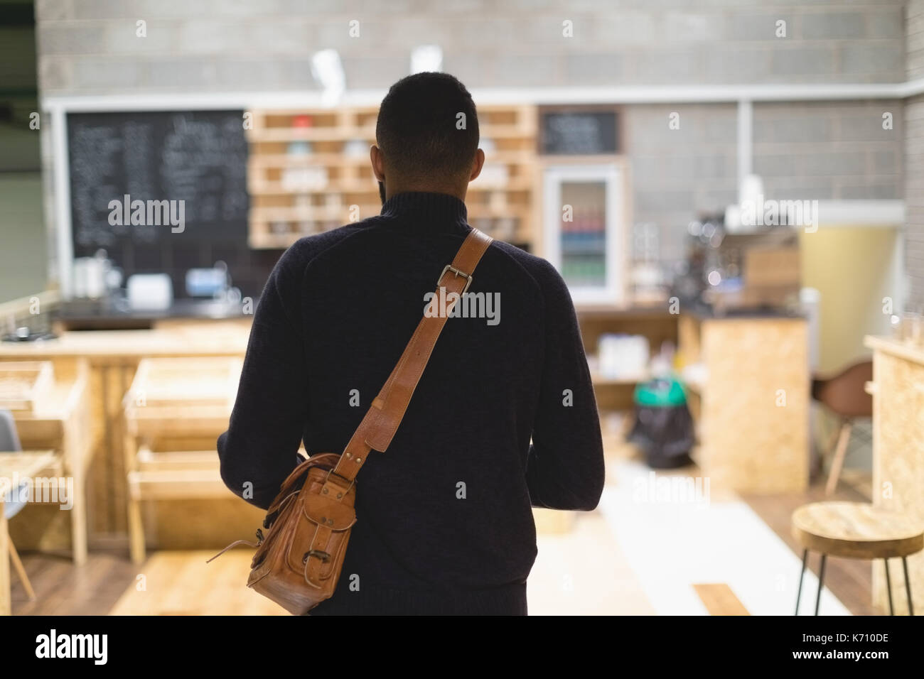 Vue arrière du jeune homme avec sac debout dans cafe Banque D'Images