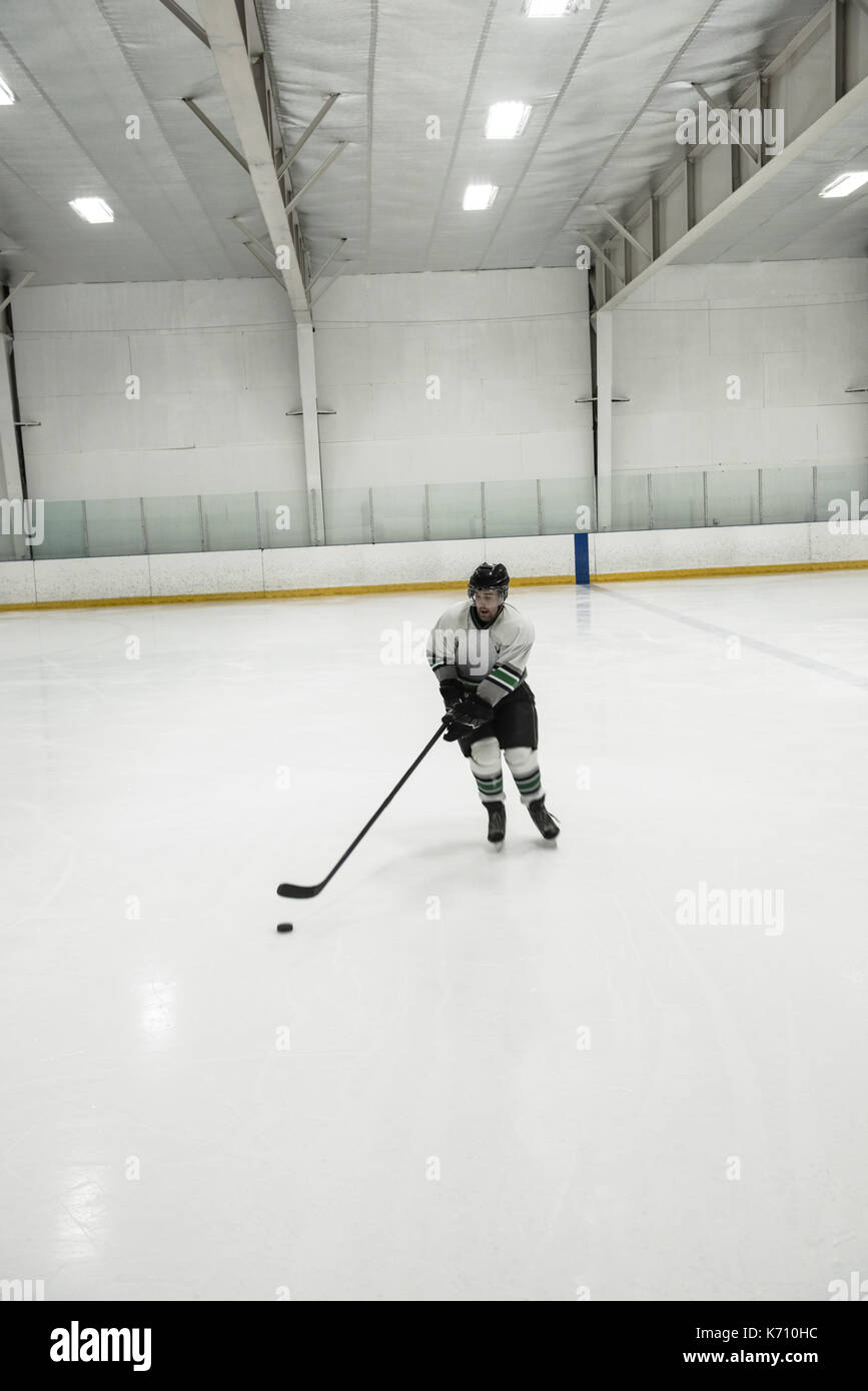 Toute la longueur de l'homme joueur pratiquant le hockey sur glace à la patinoire éclairée Banque D'Images