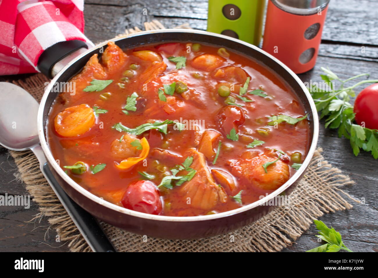 Filet de poisson cuit dans une sauce tomate avec des pois verts et tomates cerises sur une plaque sur un fond de bois sain eting. concept. Une cuisine facile. Banque D'Images