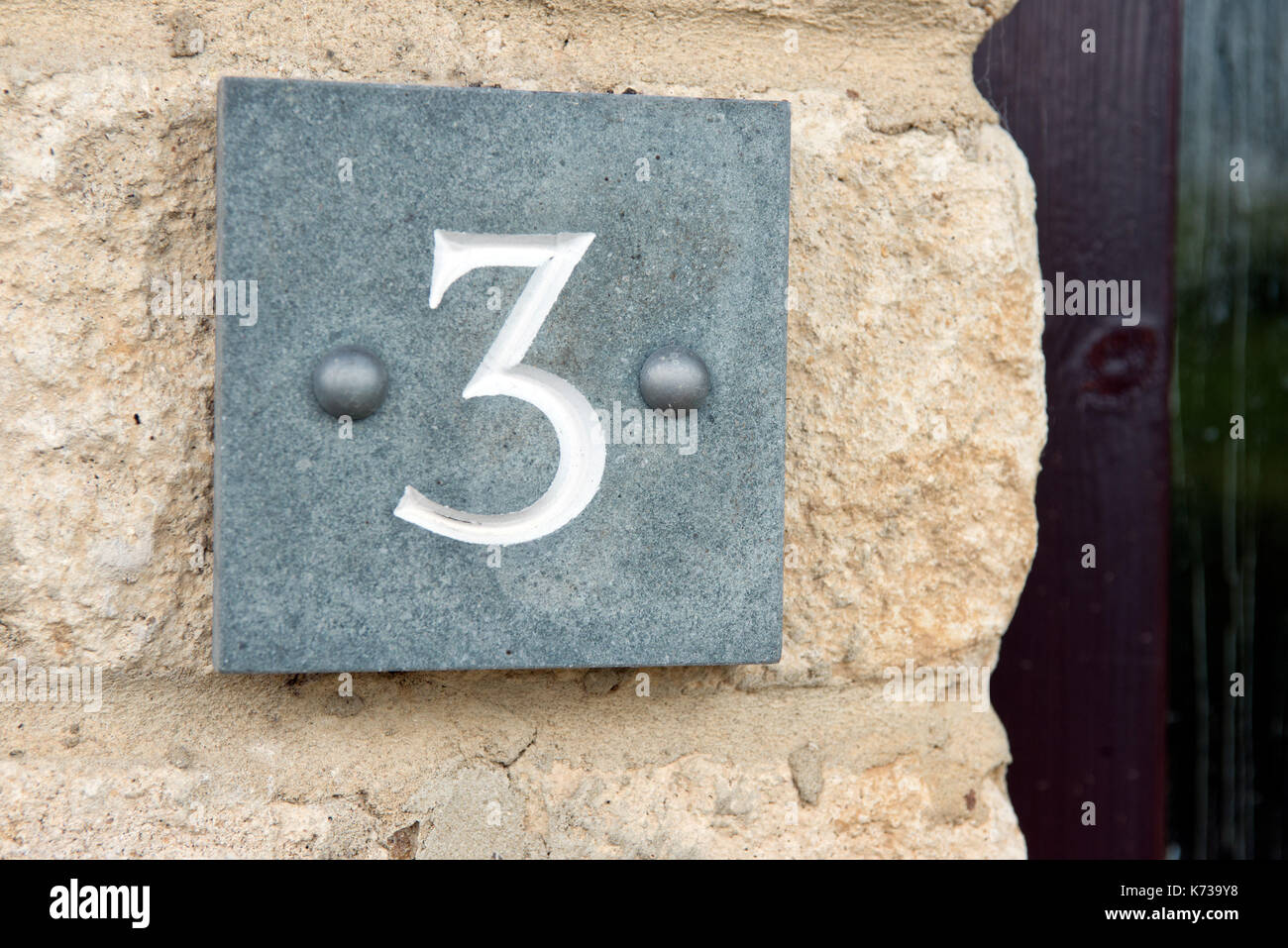 Le nombre trois gravées dans une plaque en ardoise, fixés à un mur d'identifier l'adresse d'une maison. Banque D'Images