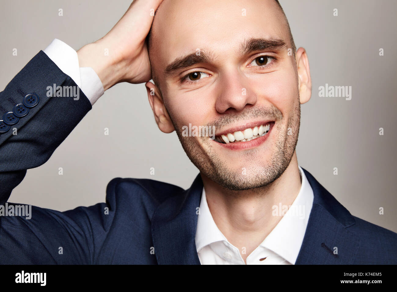 Close-up portrait of a handsome homme chauve de caresser sa tête. il sourit. fond gris. horizontale. Banque D'Images