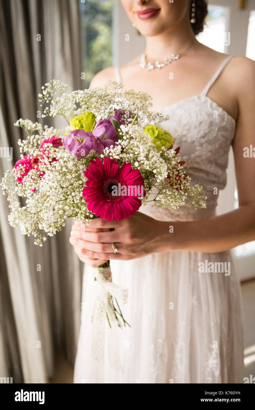 Portrait of smiling bride holding bouquet en robe de mariage tout en se tenant à la maison Banque D'Images