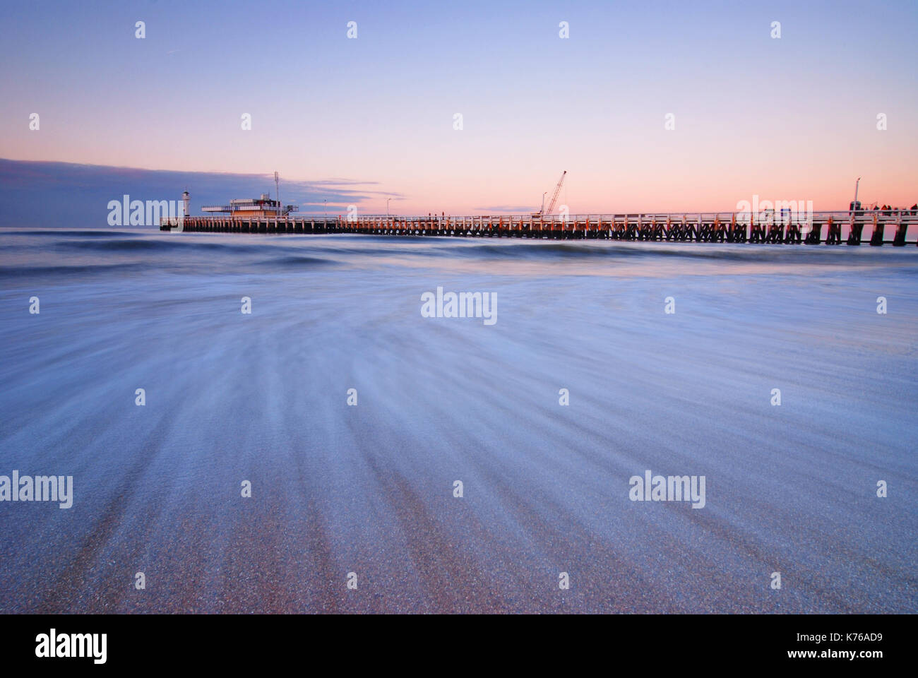 Une longue exposition de la jetée d'Ostende avec le mouvement de l'eau de la mer du Nord par la plage au coucher du soleil, en Belgique. Banque D'Images