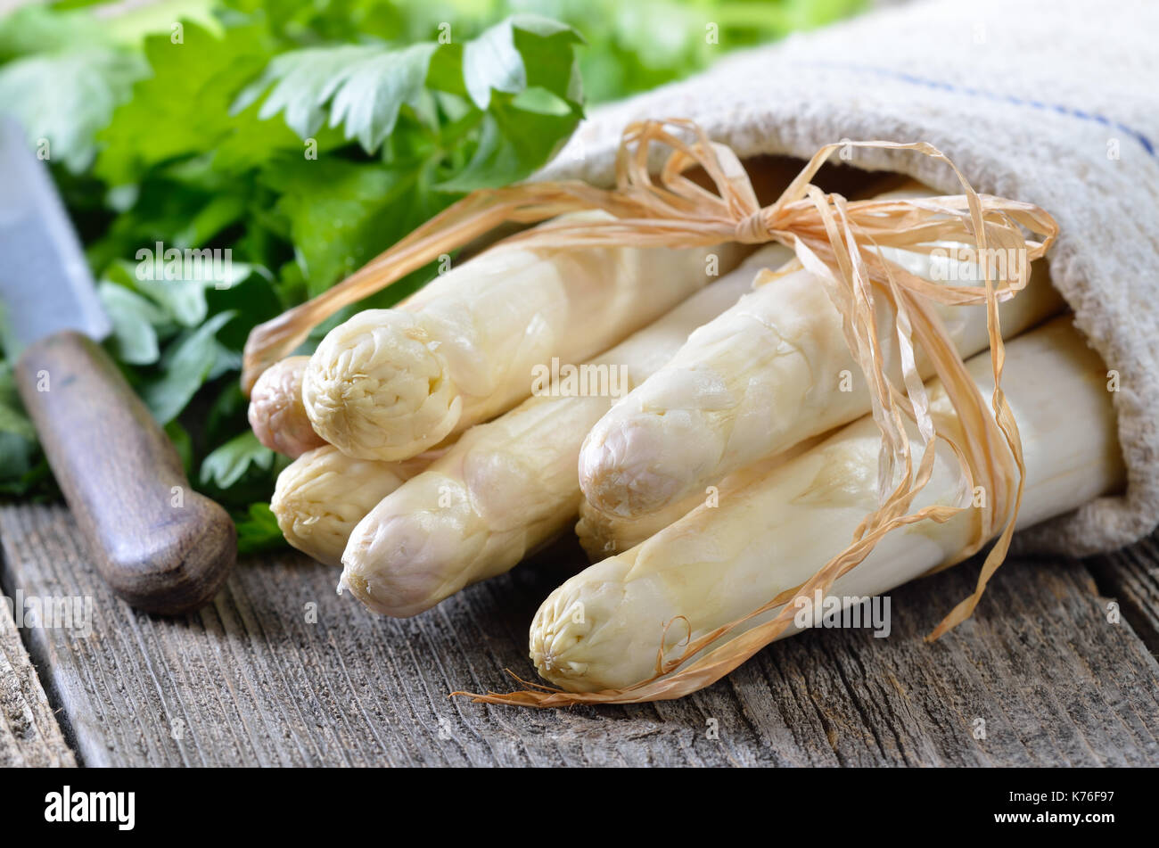 Asperges blanches fraîches sur une vieille table en bois, lié avec bast, les feuilles de céleri dans l'arrière-plan Banque D'Images