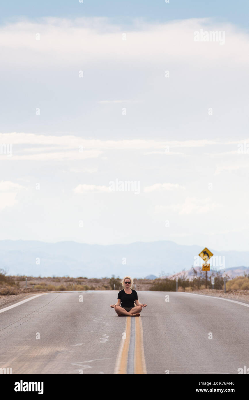 Une jeune femme est assise au milieu de la route dans le désert de Mojave Banque D'Images
