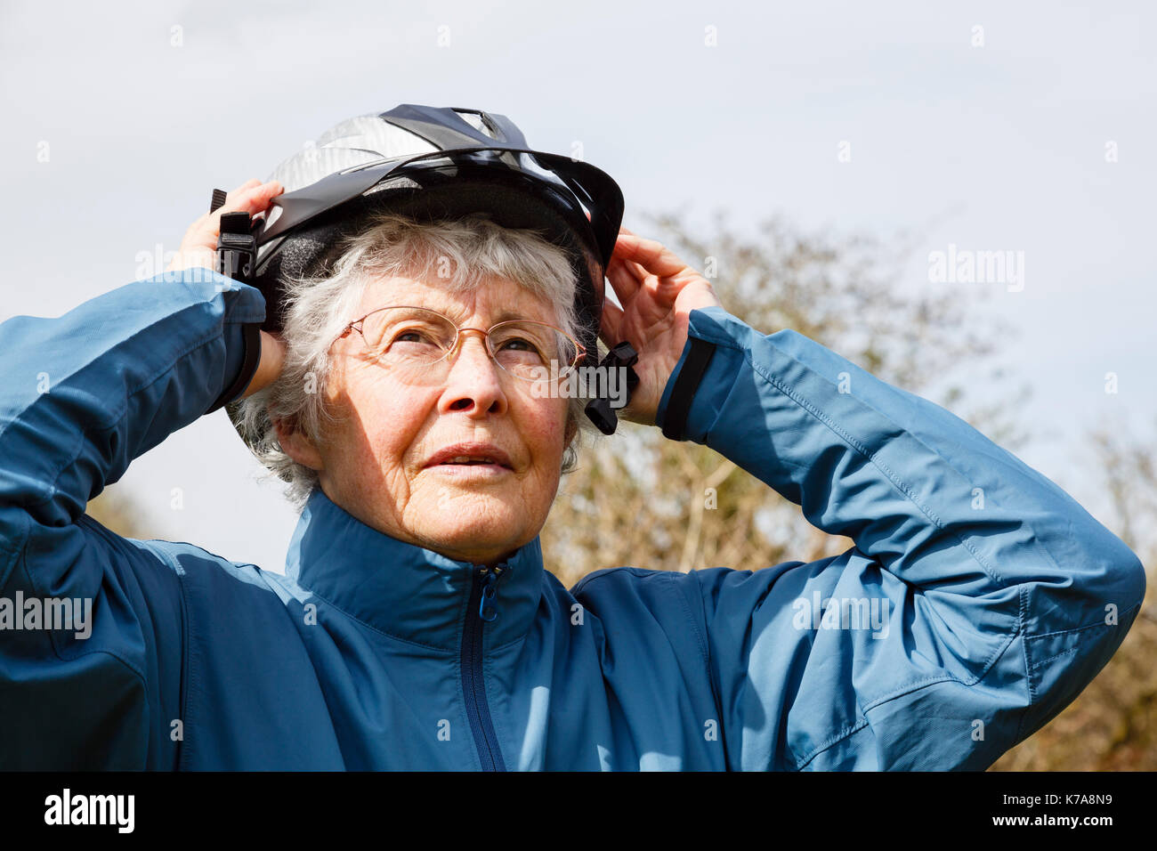 Senior retraité femme âgée la mise sur un casque de vélo se préparer à aller pour une balade en vélo pour garder la forme à la retraite. En Angleterre, Royaume-Uni, Angleterre Banque D'Images