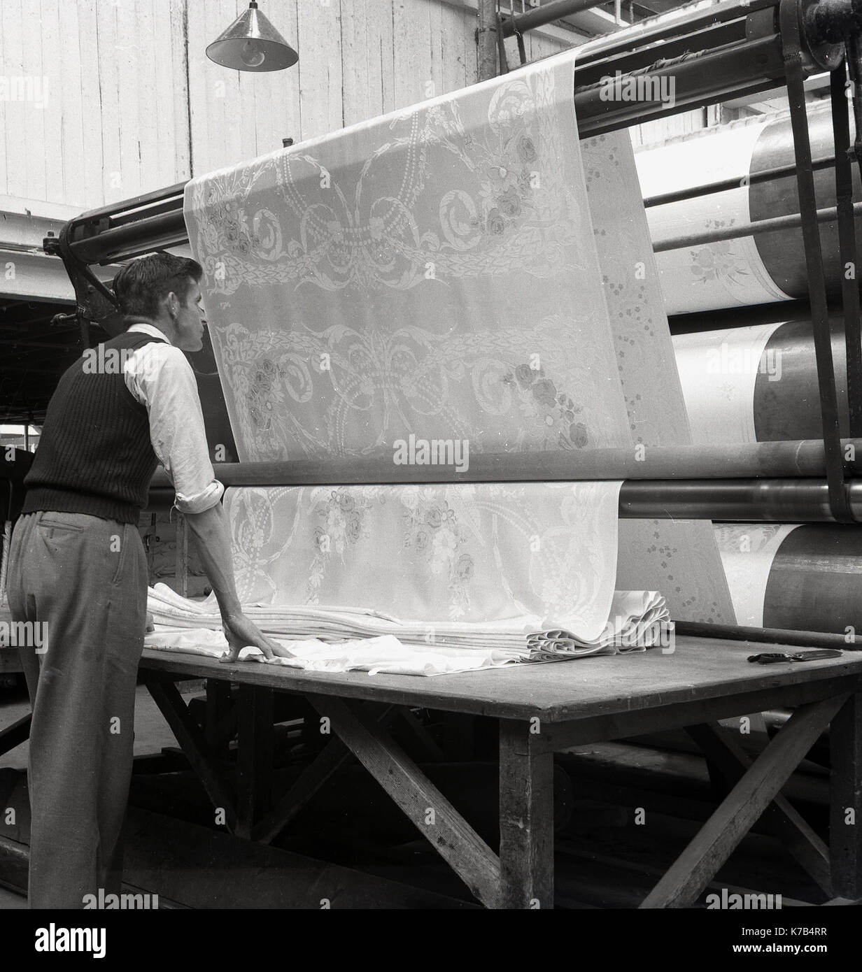 Années 1950, historique, un homme debout à côté d'une table vérifiant la qualité du linge irlandais, stocké sur de grands rouleaux, Irlande du Nord. Banque D'Images