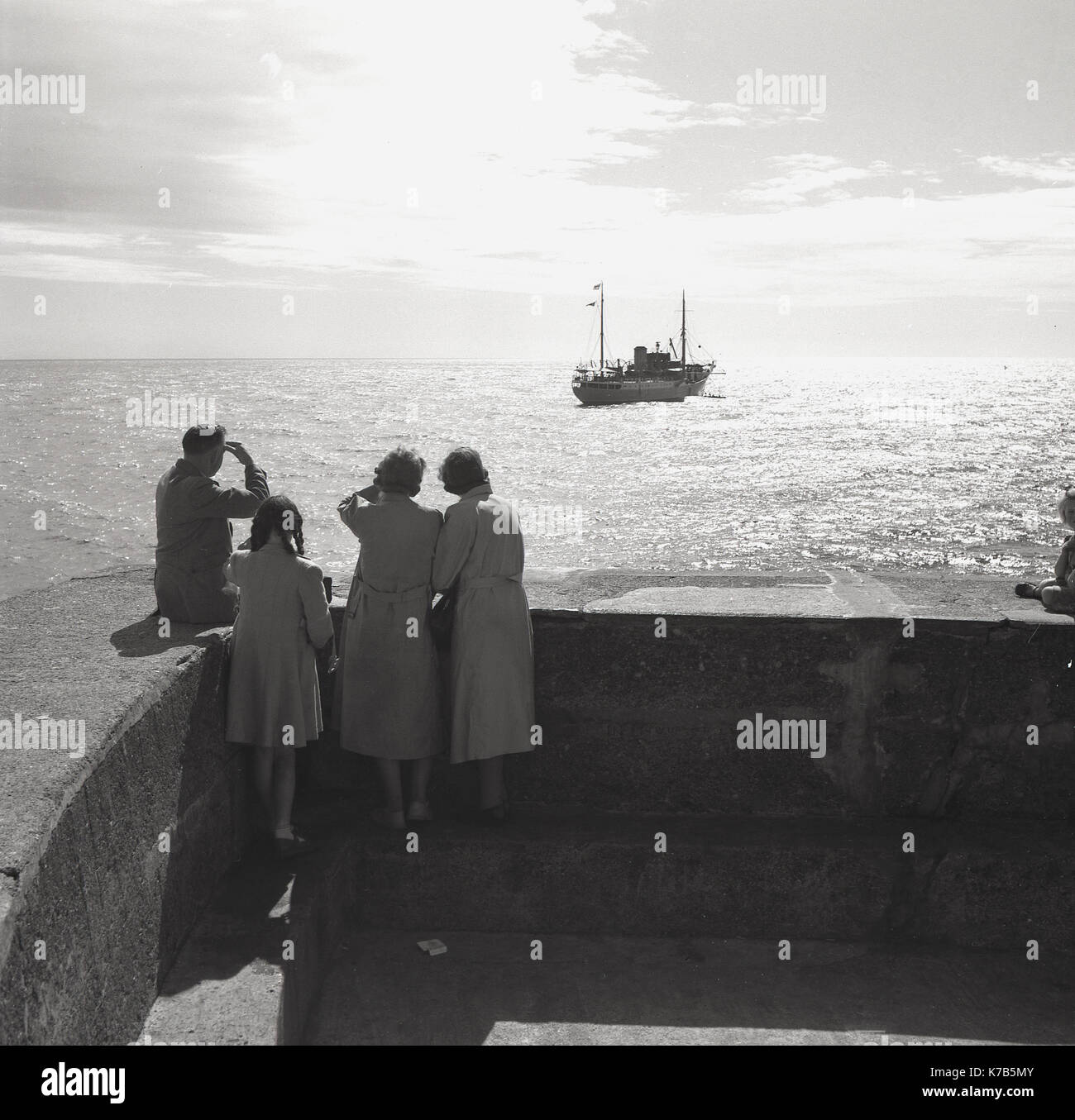 Dans les années 1950, historique, homme, femme et enfant se tiennent à la jetée en regardant les bateaux dans la baie, sachant peut-être quelqu'un qui a quitté les côtes, l'Irlande du Nord. Banque D'Images