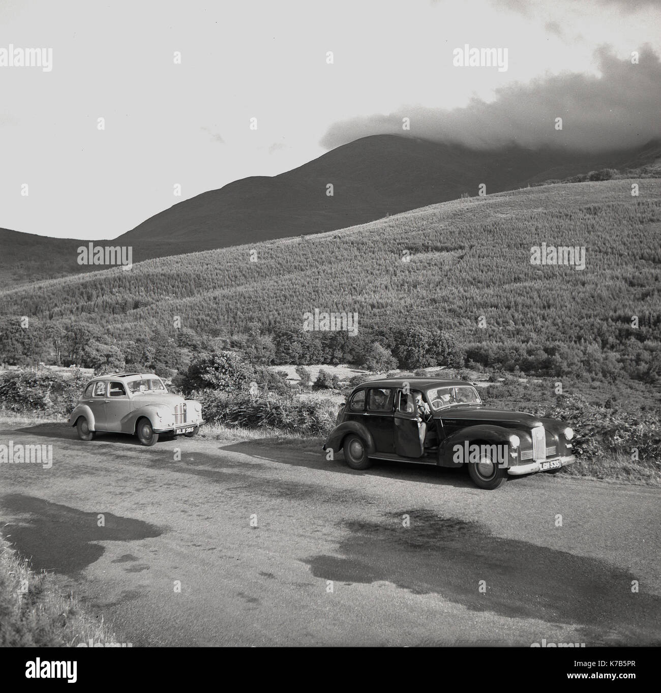 Dans les années 1950, deux voitures de berline historiques de l'époque se sont garées sur une route de campagne tranquille en Irlande du Nord, pour admirer les vues spectaculaires sur les montagnes Mourne. Banque D'Images