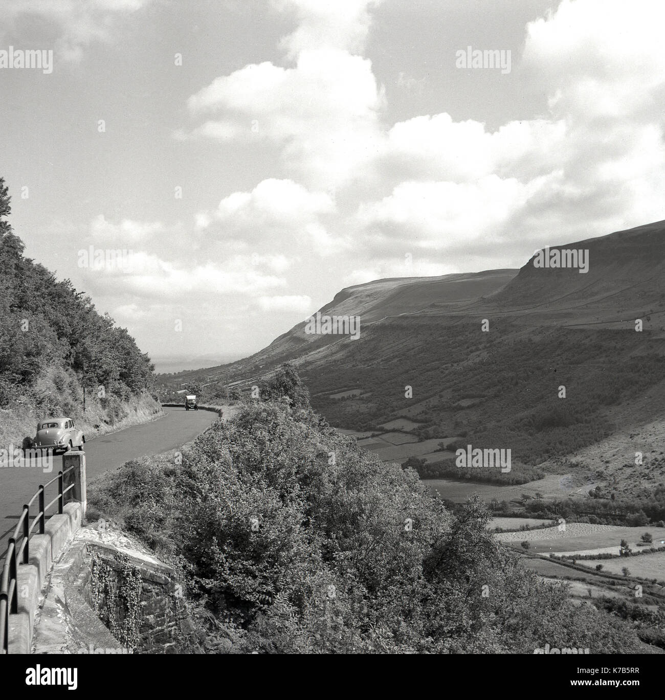 Années 1950, historique, une voiture d'Austin de construction britannique garée sur le côté d'une route de campagne, s'arrêta pour admirer la vue sur les montagnes de Morne, et les vallées environnantes à Co Down, Irlande du Nord . La chaîne de montagnes en granit des montagnes de Morne est la plus haute du pays et offre des vues spectaculaires. Banque D'Images