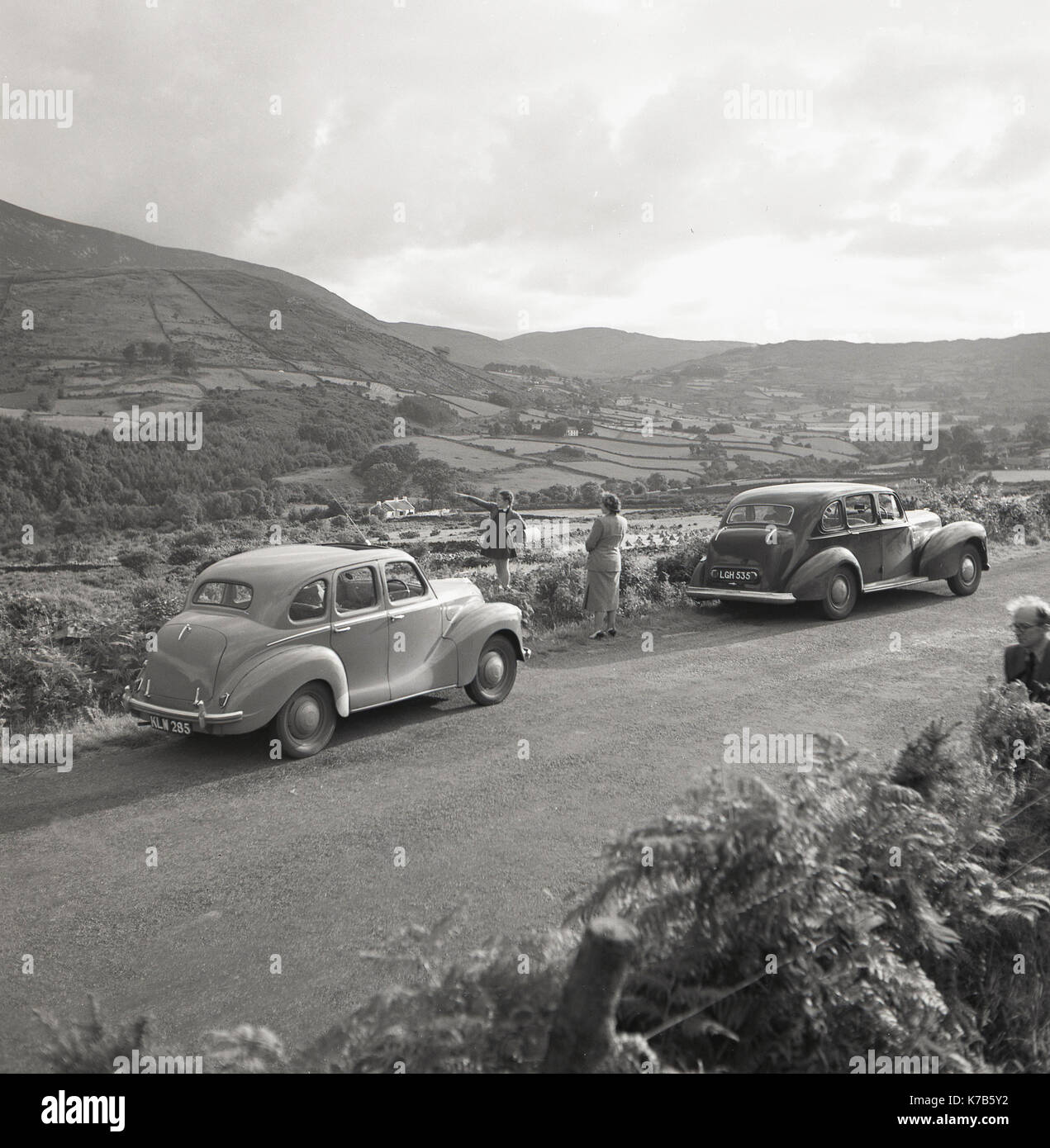 Années 1950, historique, en tournée en voiture en Irlande du Nord, une jeune fille debout sur une ruelle de campagne surplombant les montagnes de Morne pointant vers quelque chose dans la distance avec sa mère regardant. La voiture sur la gauche est une voiture britannique de l'Austn A40. Banque D'Images