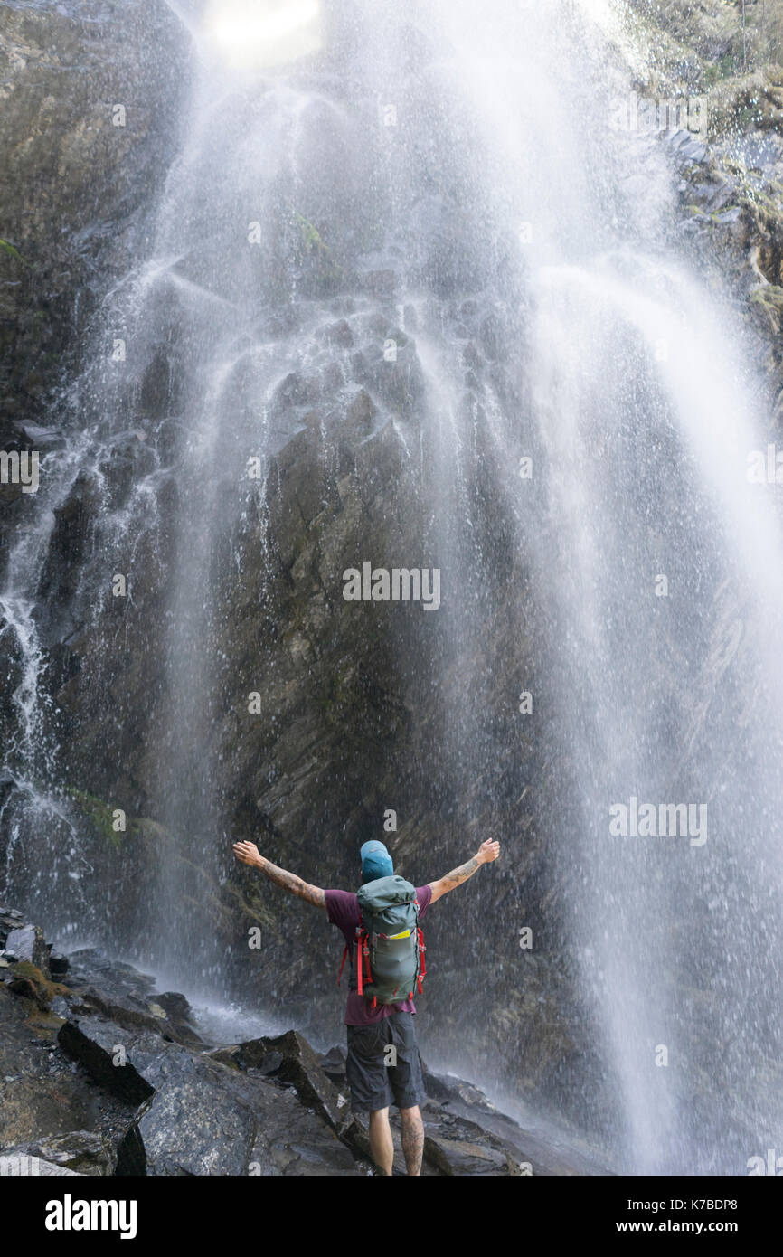 Vue arrière du hiker with arms outstretched standing against waterfall Banque D'Images
