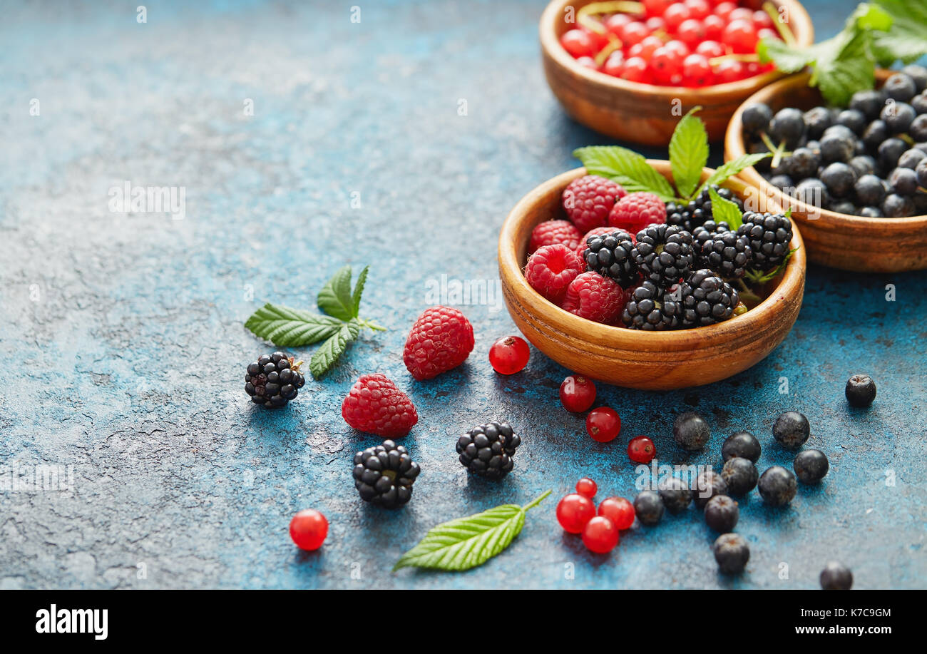 Divers les fruits d'été dans un assortiment de bols en bois. Les baies fraîches avec des feuilles sur fond de métal. Banque D'Images