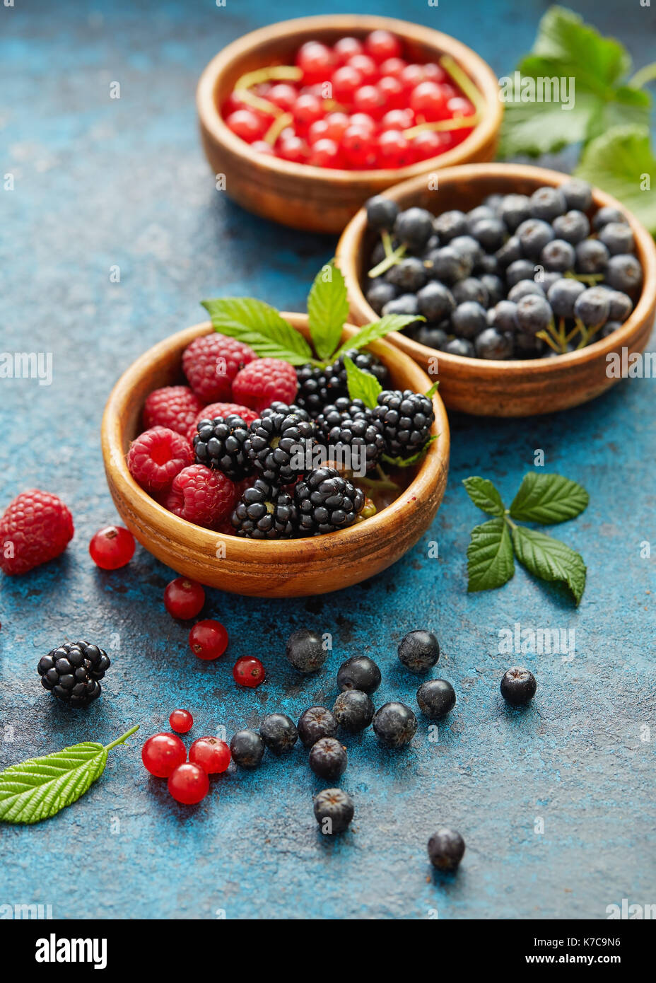 Divers les fruits d'été dans un assortiment de bols en bois. Les baies fraîches avec des feuilles sur fond de métal. Banque D'Images
