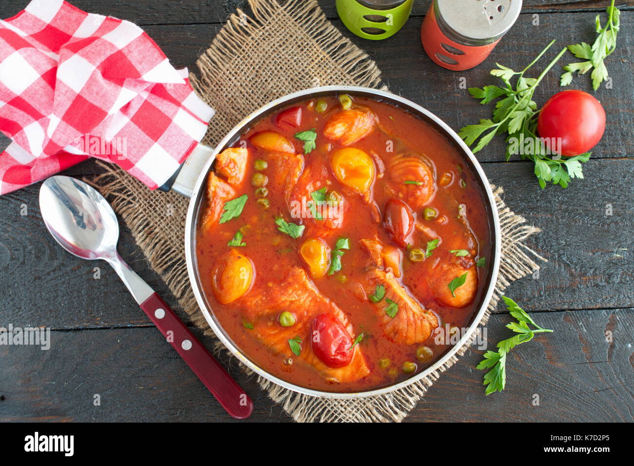 Filet de poisson cuit dans une sauce tomate avec des pois verts et tomates cerises sur une plaque sur un fond de bois sain. eaing concept. Une cuisine facile. Banque D'Images