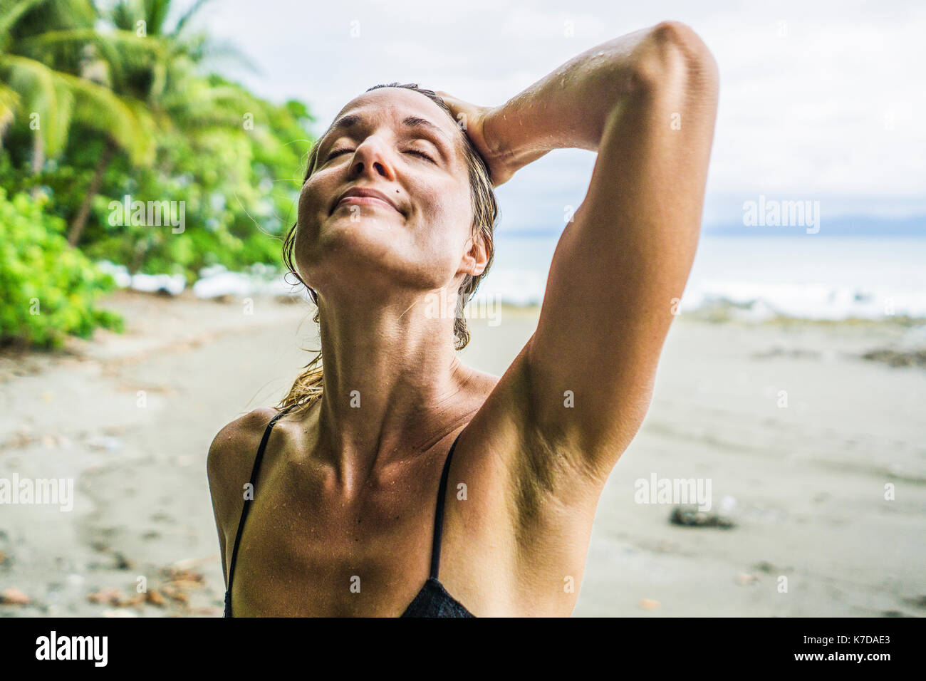 Ambiance Mid adult woman standing with main dans les cheveux humides at beach Banque D'Images