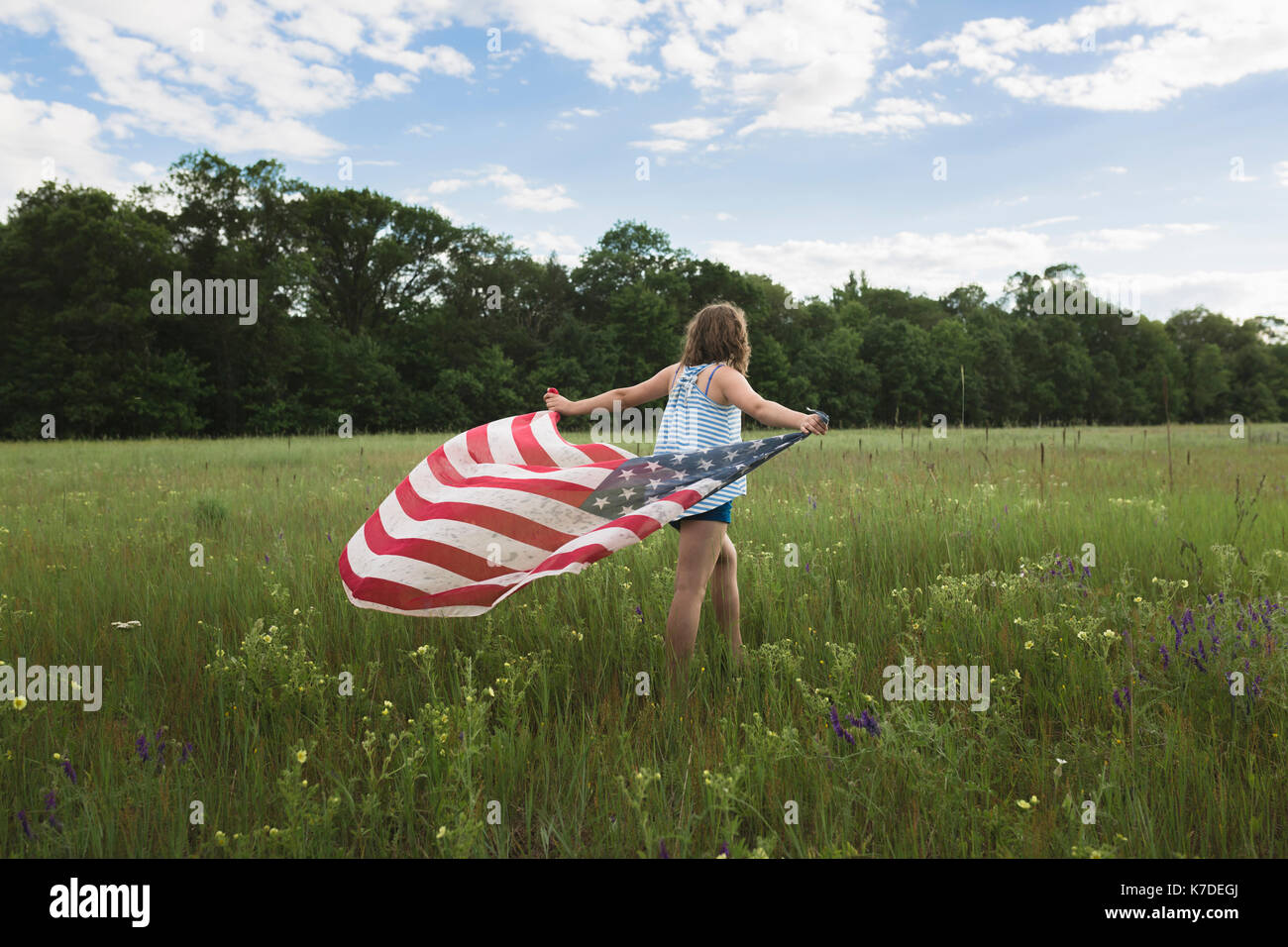 Vue arrière du girl holding American Flag en marchant sur les champs Banque D'Images