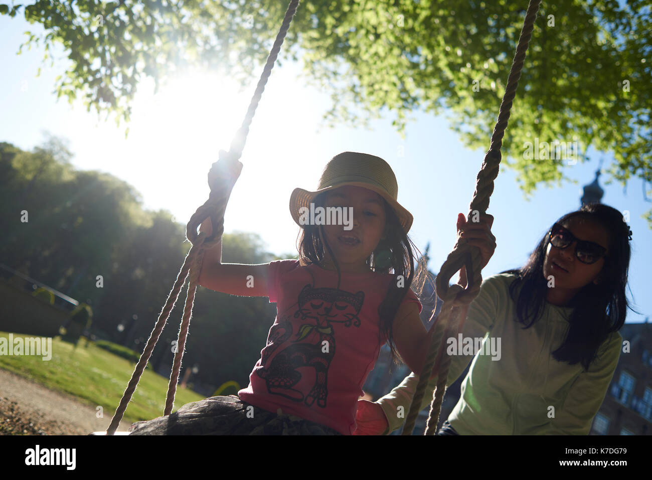 Heureux mère poussant swing corde pour fille à l'aire de jeux au cours de journée ensoleillée Banque D'Images