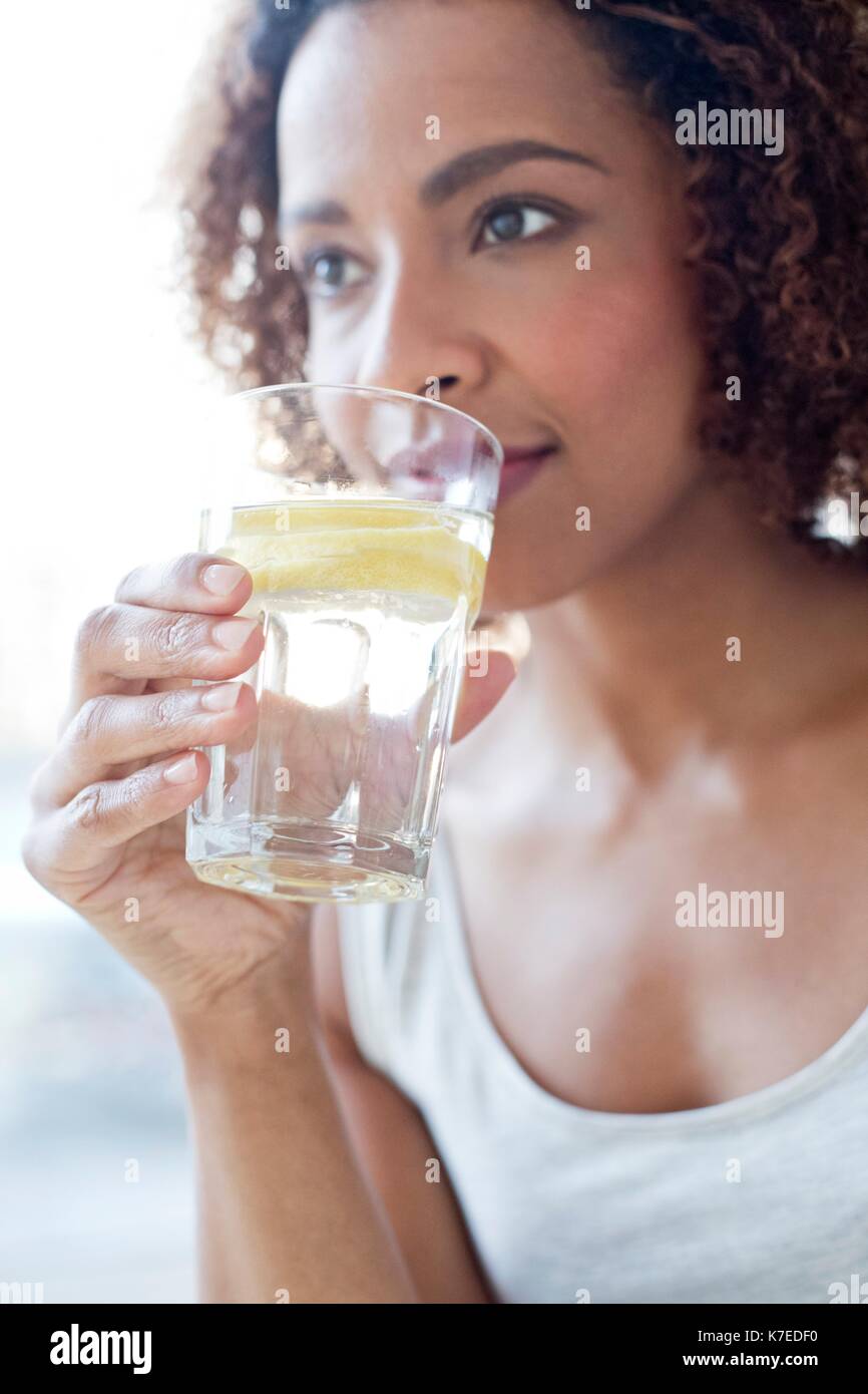 Mid adult woman eau potable avec une tranche de citron. Banque D'Images