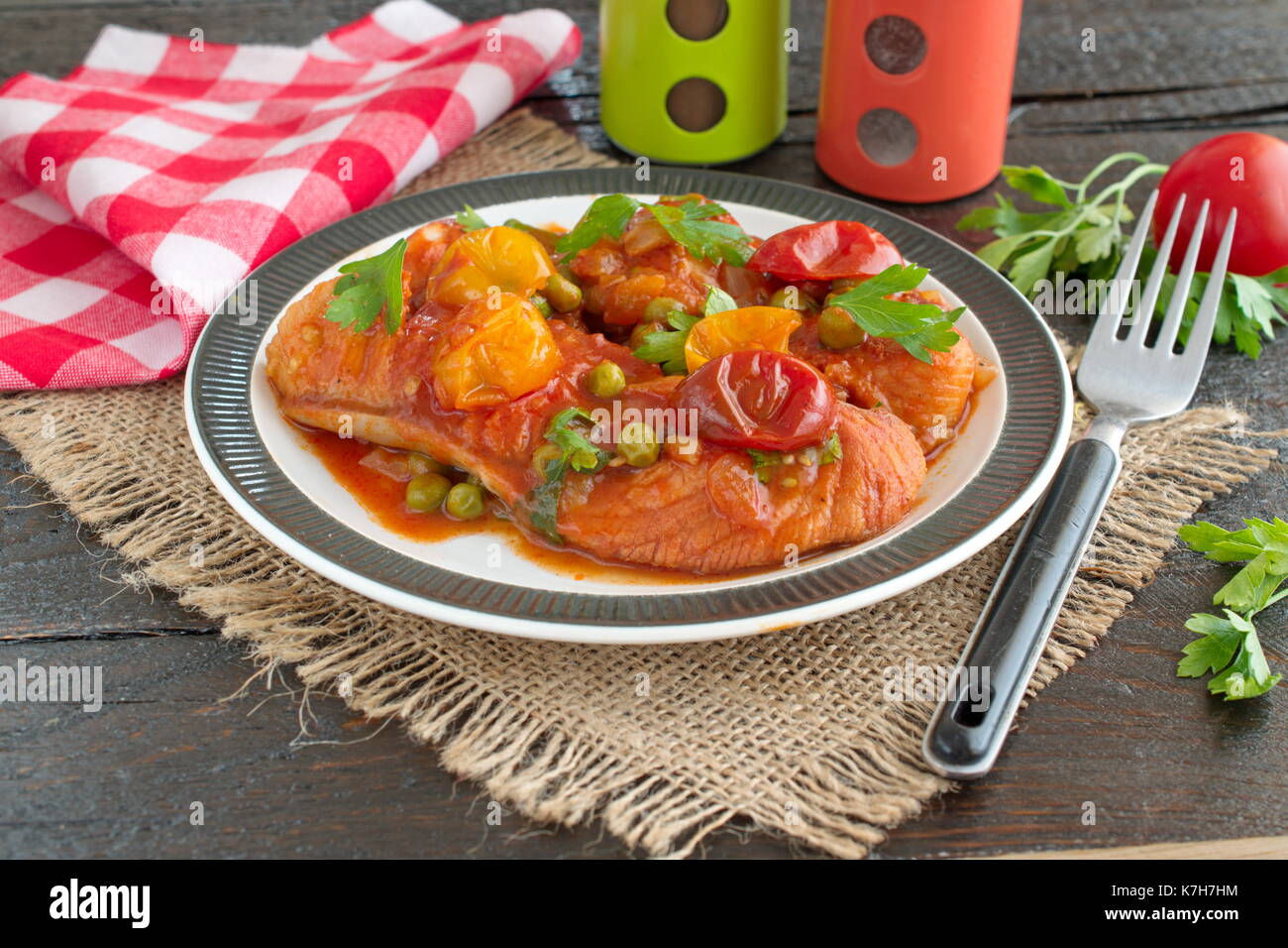 Filet de poisson cuit dans une sauce tomate avec des pois verts et tomates cerises sur une plaque sur un fond de bois sain concept eatng.. Une cuisine facile. Banque D'Images