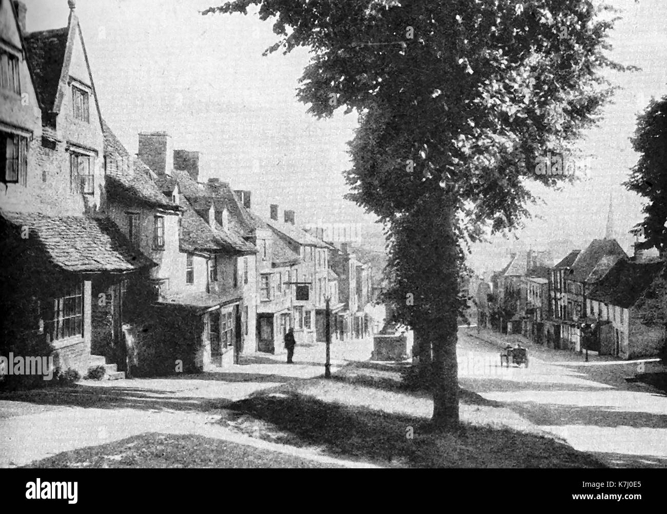 Une vieille photographie de Burford, Oxfordshire avec une seule voiture vintage descendant la rue haute Banque D'Images