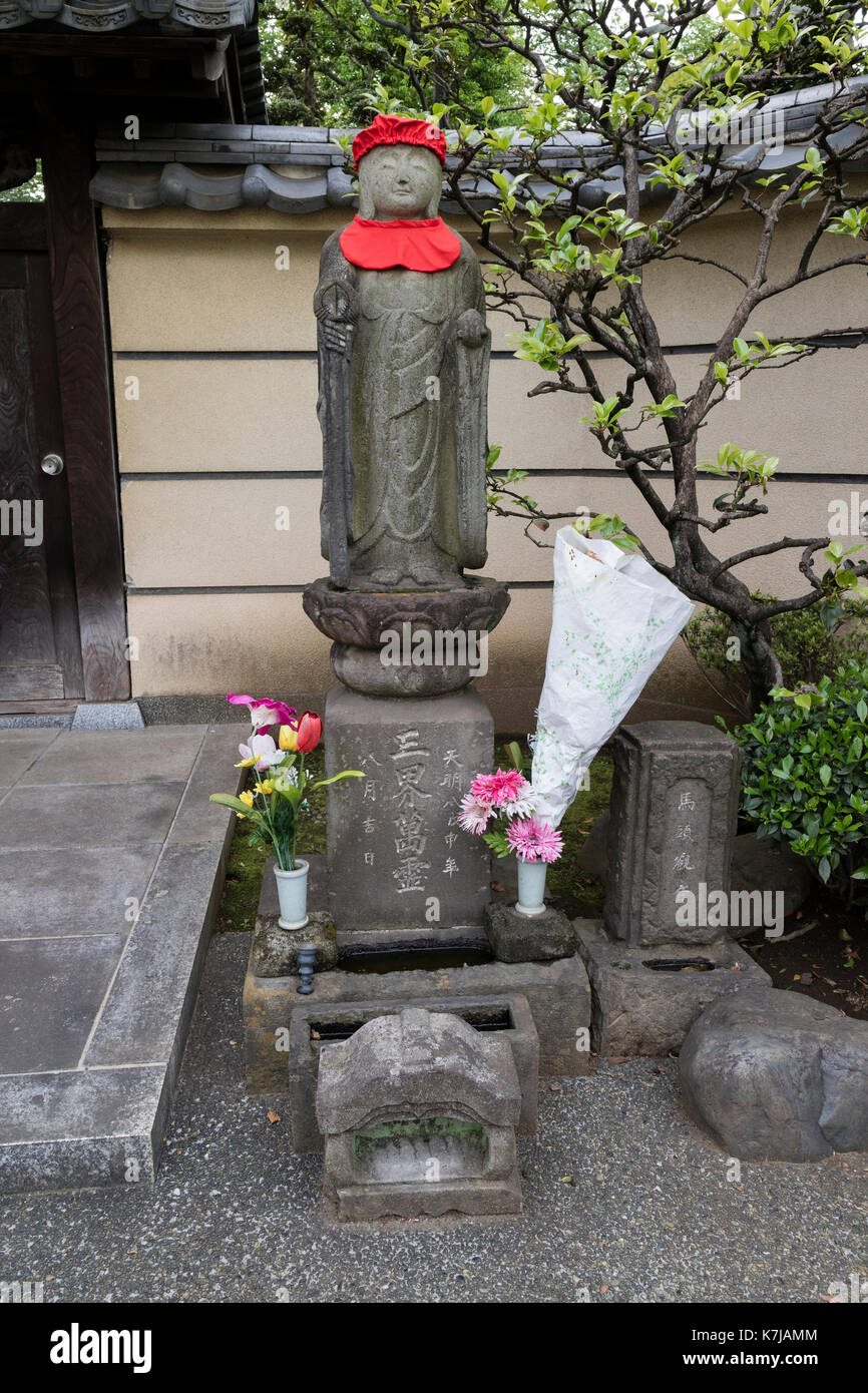 Tokyo, Japon - 15 mai 2017 : Pierre statue jizo religieuses pacifiques avec Red Hat et honoré de fleurs fraîches Banque D'Images