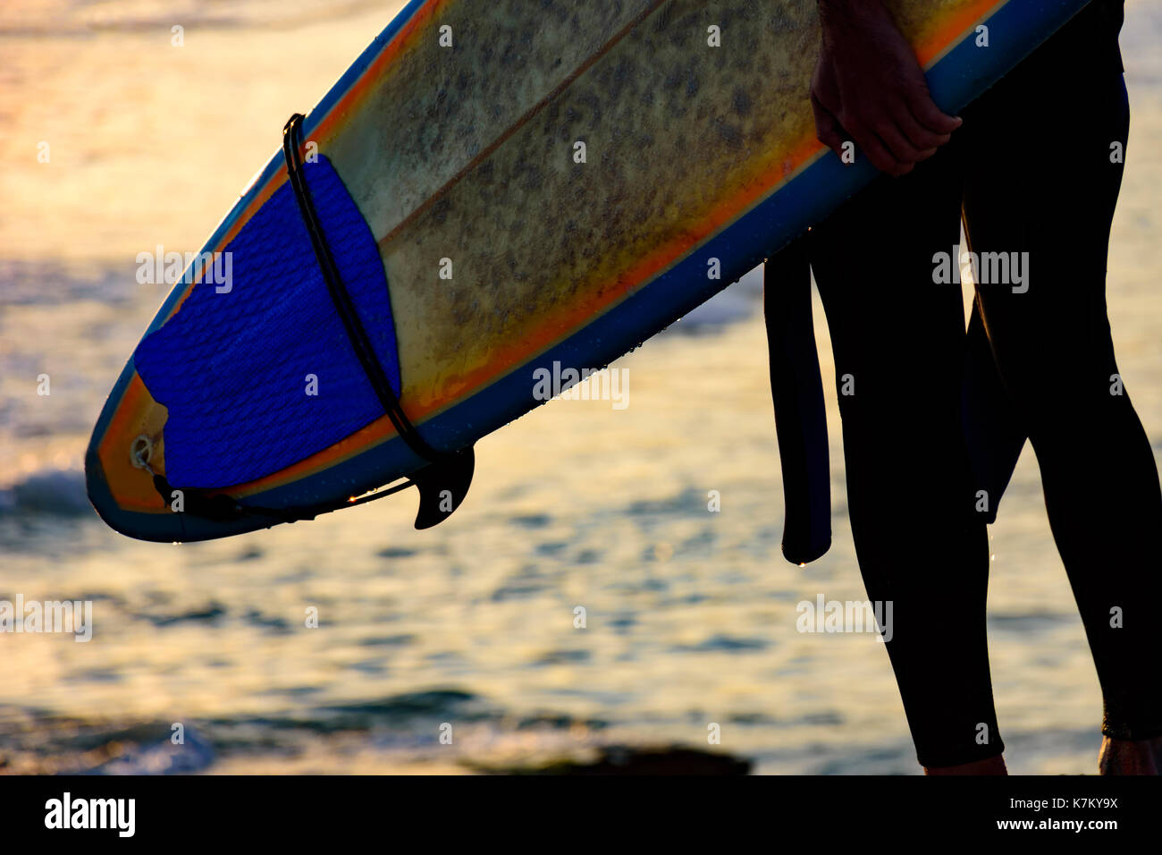 Détail de l'homme vu de dos tenant sa planche de surf en face de la mer au coucher du soleil Banque D'Images