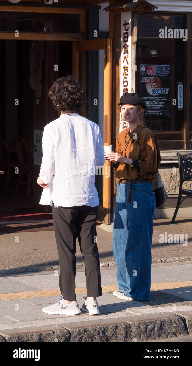 Jeune couple japonais vêtus de denim tendance , noir et blanc chemise en fin d'après-midi debout sur le trottoir à la recherche et à l'écart de l'appareil photo. Banque D'Images