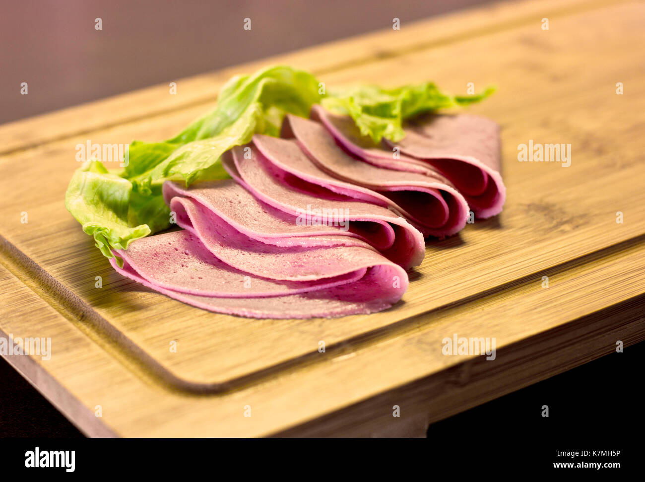 Minces tranches de saucisse avec salade verte sur planche de bois Banque D'Images