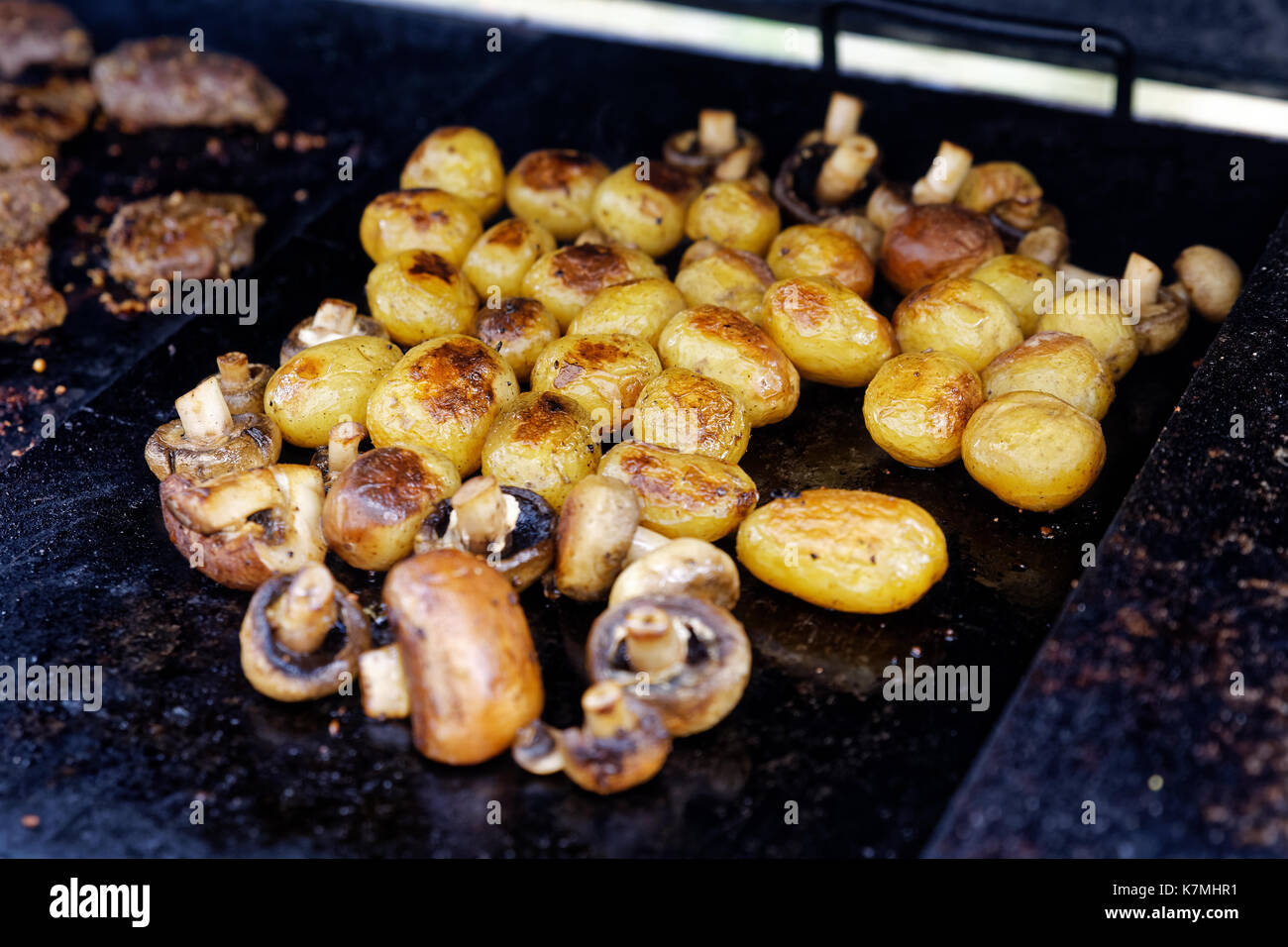 Champignons grillés et de pommes de terre entières sur un grill extérieur. Banque D'Images