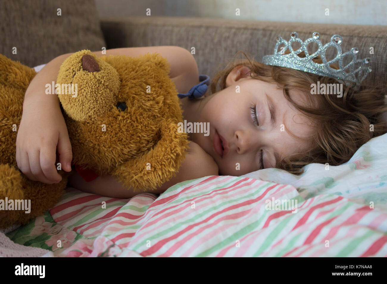 Close-up portrait of little girl sleeping in bed. Jeune fille avec une couronne de princesse sur la tête de lit en serrant un ours en peluche jouet, concept de rêves pacifiques Banque D'Images