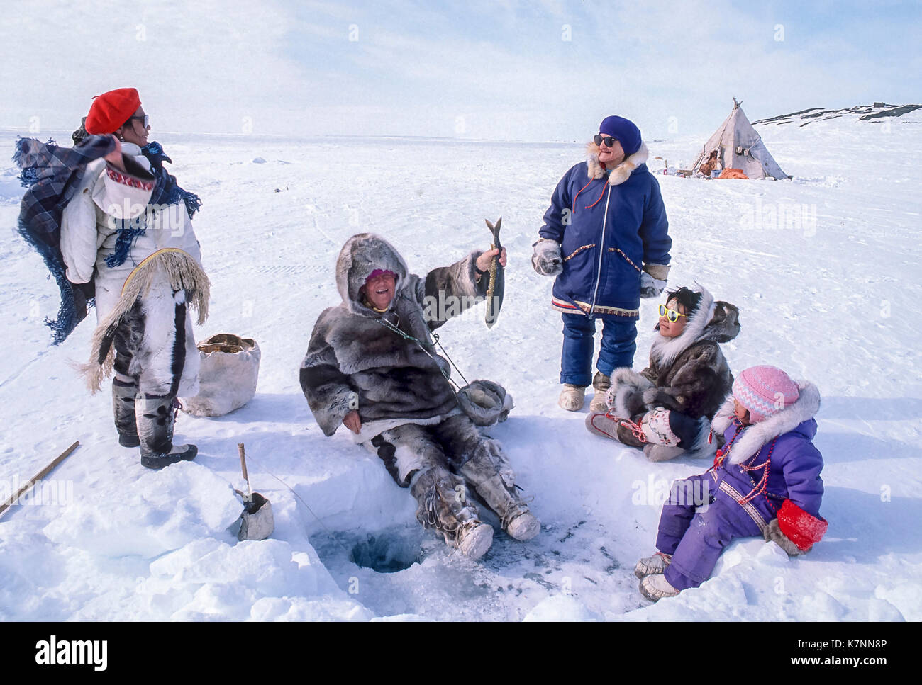 Visiteur vêtu de vêtements traditionnelle de caribou, tente à la pêche au camp à l'extérieur de Baker Lake, Nunavut, Canada. Des aînés inuits et des enfants inuits sont réunis autour du trou de pêche. Banque D'Images