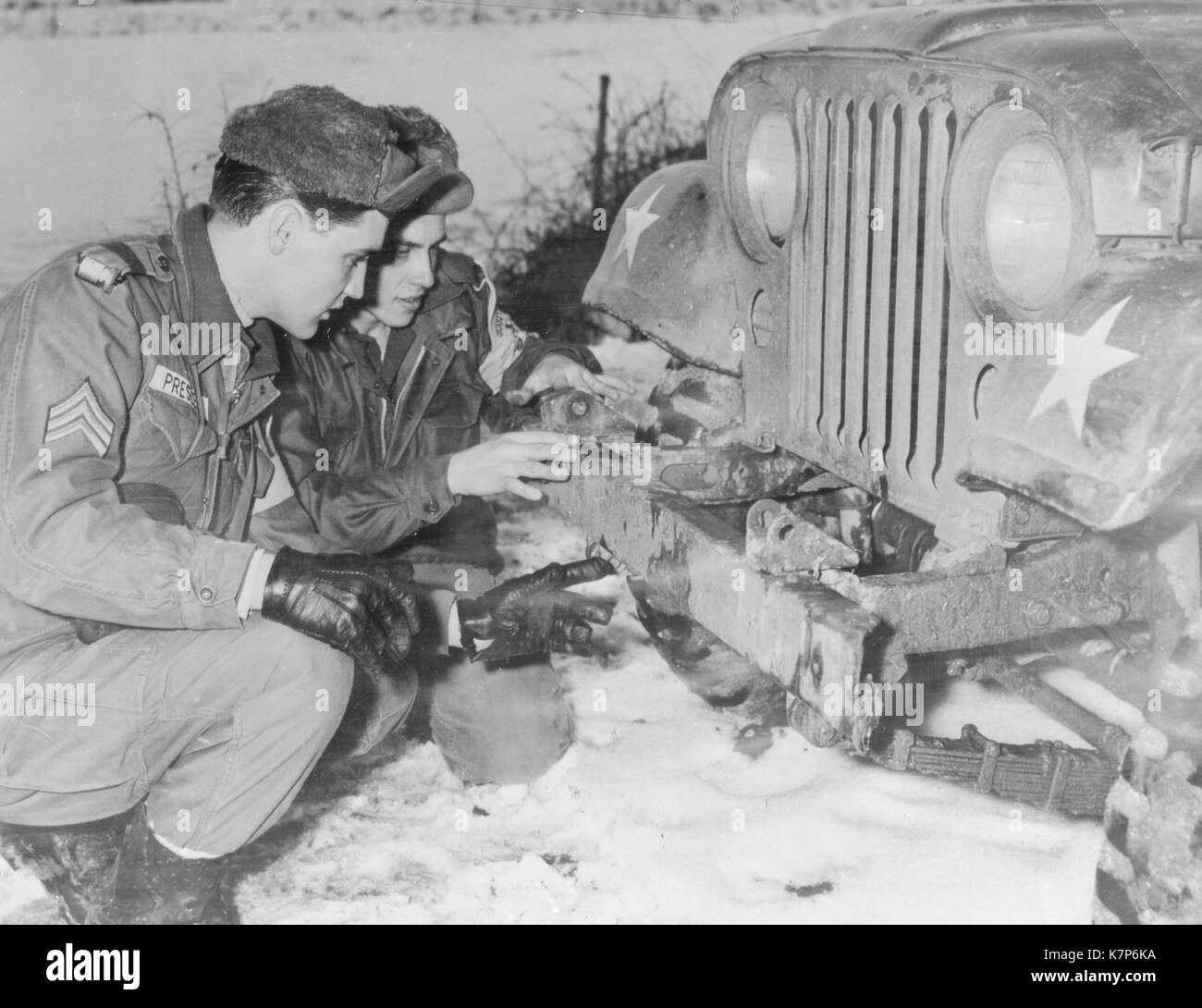 1960 - Le Sgt Elvis Presley vérifie avec d'autres armures jeep 32e scout Pvt Lonnie Wolfe, conducteur de Presley's jeep. Banque D'Images