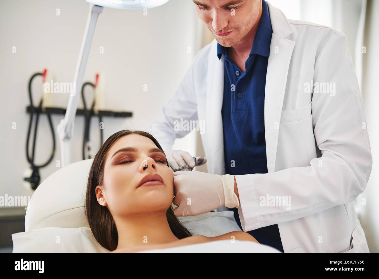Médecin homme d'effectuer des injections de botox à la joue d'une jeune femme allongée sur une table dans une clinique de beauté Banque D'Images