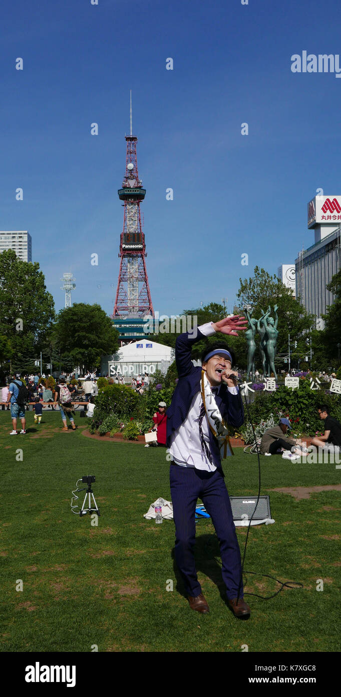 Photo verticale de jeunes japonais un homme portant un costume bleu, le chant et la danse de odori park sur journée ensoleillée avec sapporo tower en arrière-plan. Banque D'Images