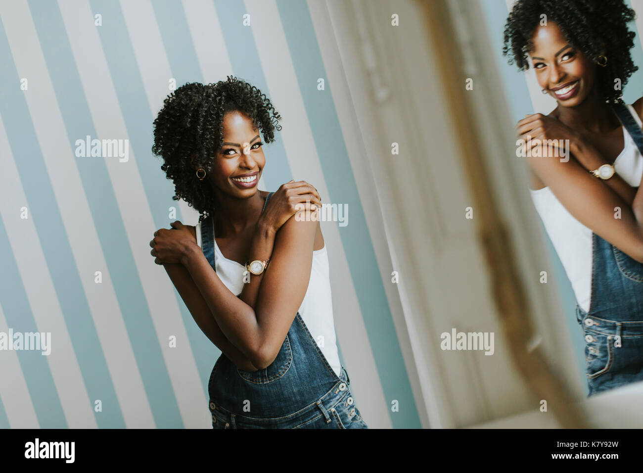 Pretty african american woman posing in jeans pantalons par le mur dans la chambre Banque D'Images