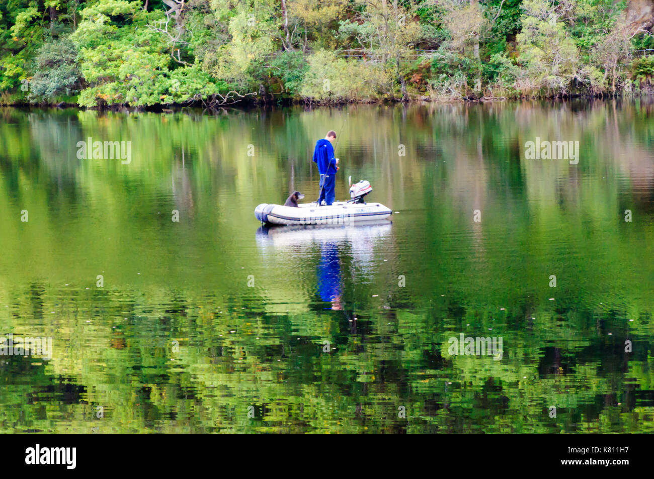 Loch Ard, Ecosse, Royaume-Uni. 17 Septembre, 2017. Météo France : Un homme d'un petit bateau de pêche avec son chien, la journée calme offre des réflexions sur la surface de l'eau. Loch Ard est un organe de l'eau douce dans le parc national du Loch Lomond et des Trossachs du district de Stirling en Écosse. Credit : Skully/Alamy Live News Banque D'Images