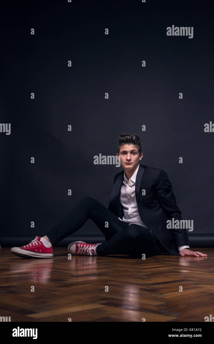 Un jeune adolescent, fond noir, studio, assis posant, vêtements, un costume officiel Banque D'Images